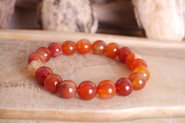 Bracelet en pierre naturelle cornaline de couleur orange perles de taille 10mm posé sur une planche de bois