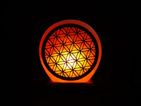 Lampe en cristal de sel de face sur fond noir. Sa forme est un disque épais avec une trame en bois ajourée en forme de fleur de vie collée dessus