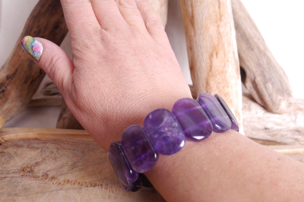 Bracelet améthyste perles plaquettes de forme rectangulaire. Il présenté sur un poignet sur fond bois
