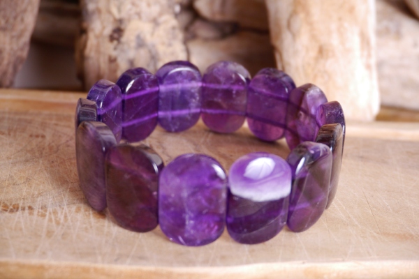 Bracelet améthyste perles plaquettes de forme rectangulaire. Il posé sur une plaque de bois sur fond bois