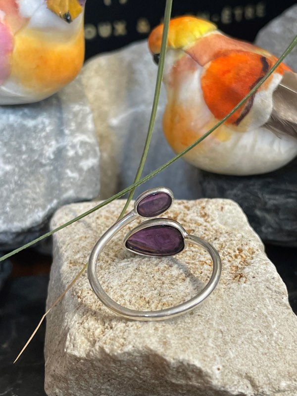Bague en argent et 2 pierres d’améthyste violette, une plus grosse forme goutte et l’autre plus petite forme ovale. Bague posée sur pierre blanche décor nature . Photo prise de l’arrière pour voir le dessous de la pierre