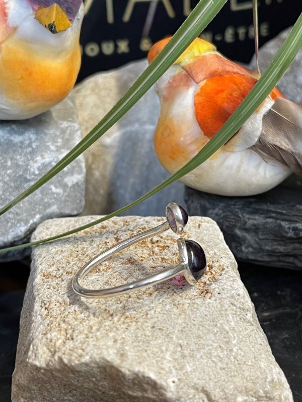 Bague en argent et 2 pierres d’améthyste violette, une plus grosse forme goutte et l’autre plus petite forme ovale. Bague posée sur pierre blanche décor nature . Photo prise de profil droit