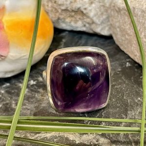Bague argent et pierre améthyste violet de forme carré. Bague posée sur des pierres noires et blanches. Photo prise de face