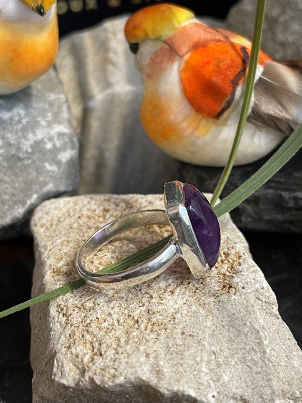 Bague argent et pierre améthyste rectangle posée sur une pierre blanche décor nature. Photo prise de profil droit