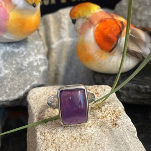 Bague argent et pierre améthyste rectangle posée sur une pierre blanche décor nature. Photo prise de face