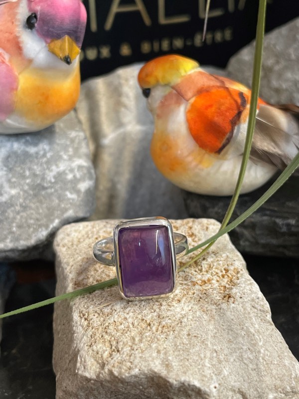 Bague argent et pierre améthyste rectangle posée sur une pierre blanche décor nature. Photo prise de face