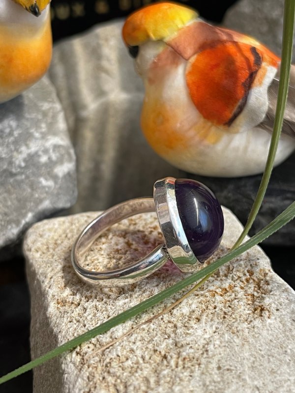 Bague argent et pierre améthyste violette forme ronde. Bague posée sur une pierre sur décor nature. Photo prise de profil droit