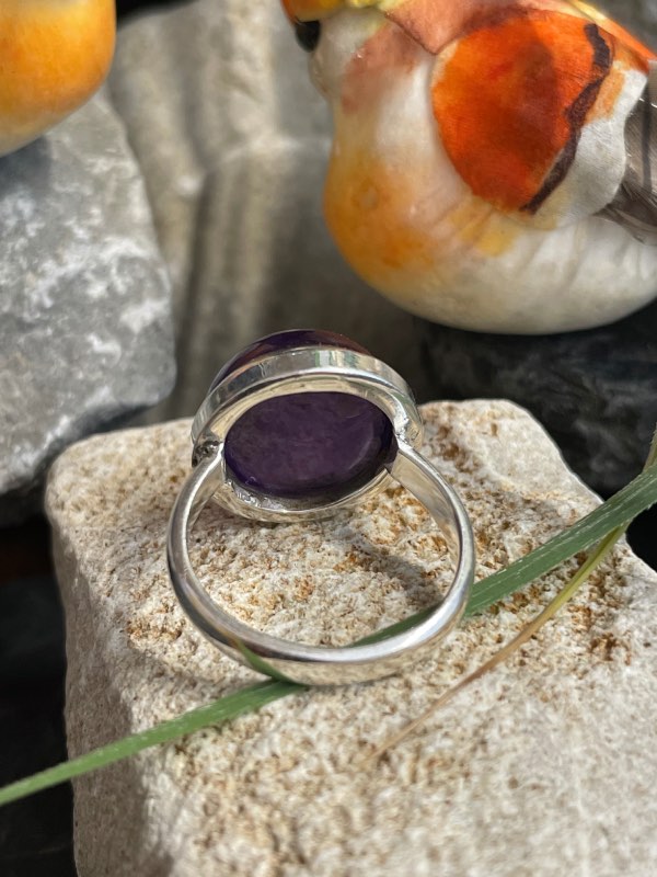 Bague argent et pierre améthyste violette forme ronde. Bague posée sur une pierre sur décor nature. Photo prise de l’arrière pour montrer le dessous de la pierre
