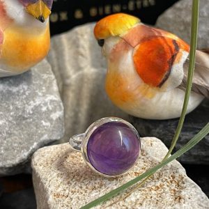 Bague argent et pierre améthyste violette forme ronde. Bague posée sur une pierre sur décor nature. Photo prise de face