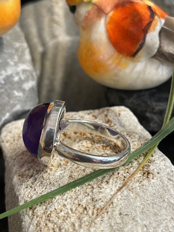 Bague argent et pierre améthyste violette forme ronde. Bague posée sur une pierre sur décor nature. Photo prise de profil gauche