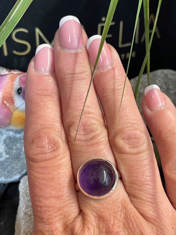 Bague argent et pierre améthyste violette forme ronde. Bague portée sur une main sur décor nature. Photo prise de face