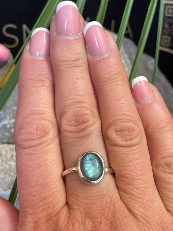 Bague en argent 925 et labradorite de couleur bleu/vert clair de forme ovale. Elle est portée sur une main avec un fond naturel. La photo est prise de face
