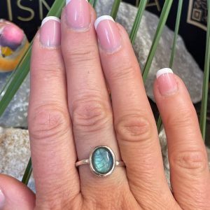 Bague en argent 925 et labradorite de couleur bleu/vert clair de forme ovale. Elle est portée sur une main avec un fond naturel. La photo est prise de face