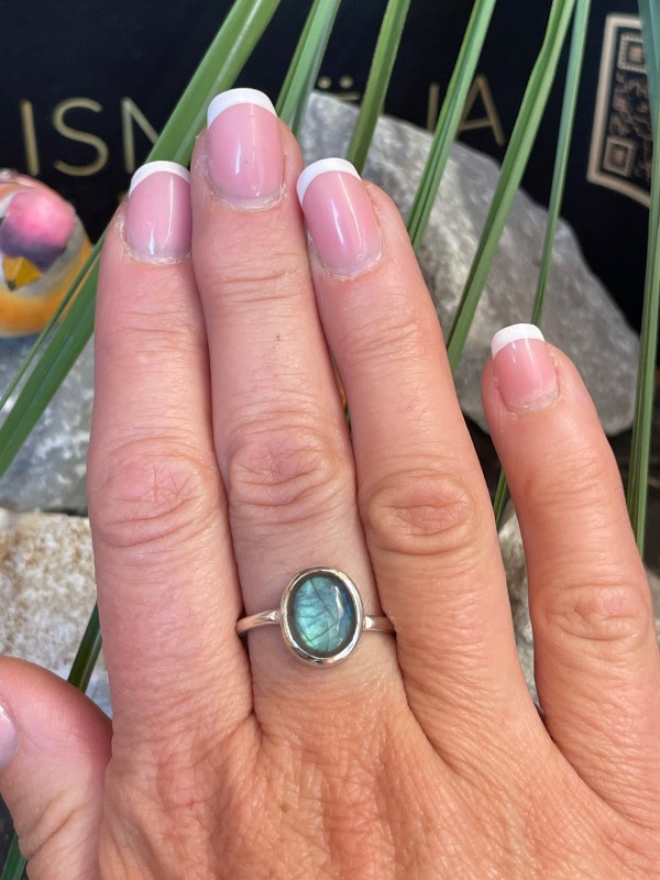 Bague en argent 925 et labradorite de couleur bleu/vert clair de forme ovale. Elle est portée sur une main avec un fond naturel. La photo est prise de face
