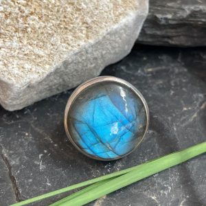 Bague argent et labradorite couleur bleu très lumineux de forme ronde. Bague posée sur une pierre noire sur fond nature. Photo prise de face
