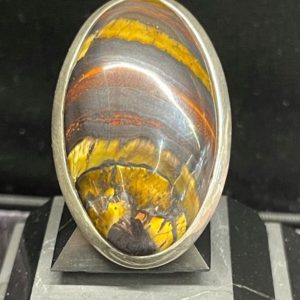 Bague en argent et œil de fer de forme gris ovale, posée sur une pyramide de Shungite sur fond noir. Photo prise de face