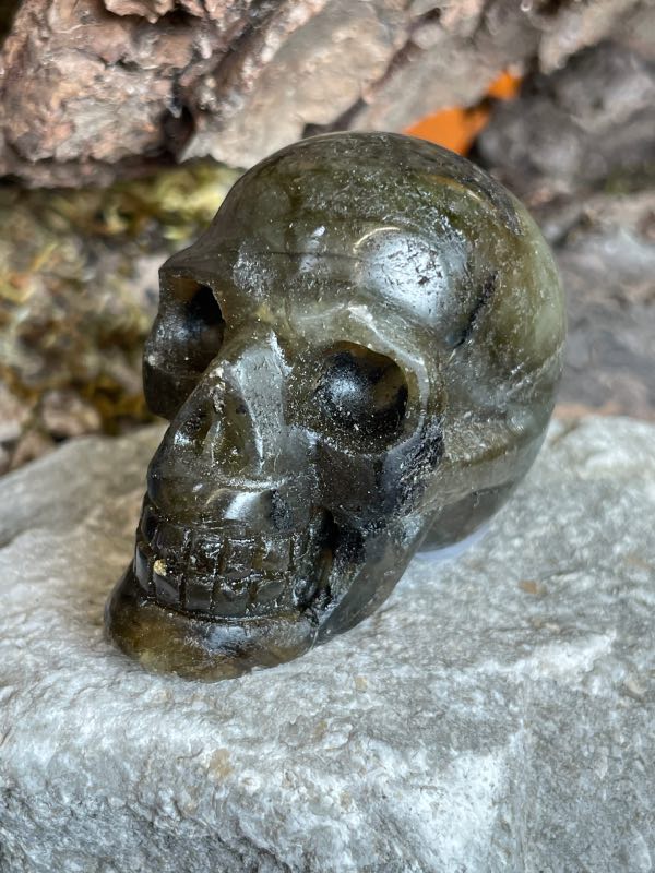 Crâne en pierre labradorite posée sur une pierre blanche. Photo prise de profil gauche