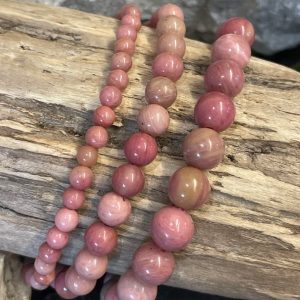Bracelet rhodonite Rose, perles 10, 8 et 6mm. Bracelet enfilé sur un bois flotté, photo prise sur fond naturel en pierres